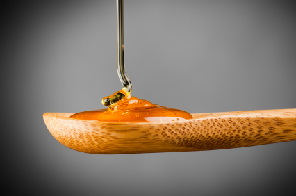 Pure golden manuka honey pouring over a wooden bamboo spoon